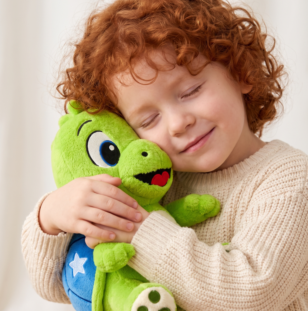 Meisje dat de groene schildpadknuffel Tobi glimlachend tegen haar wang drukt