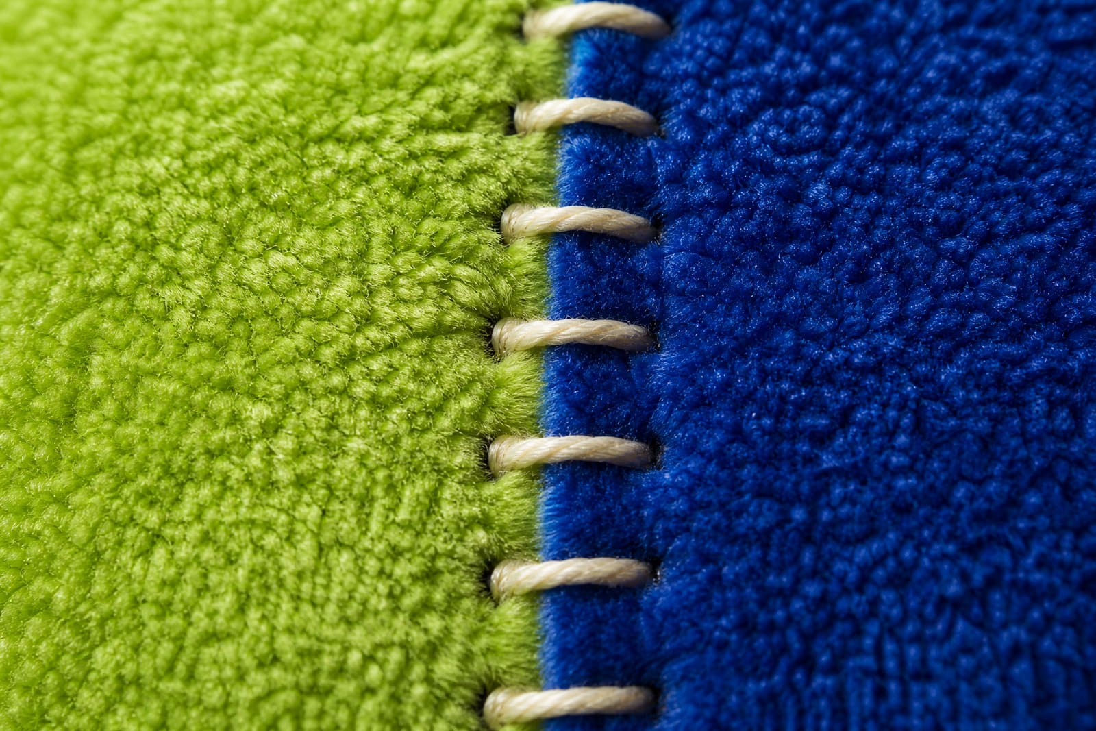 Macro-opname van een stiksel dat groene en blauwe pluche verbindt